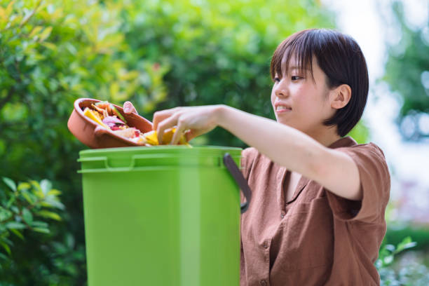 "A woman holding a plate of food scraps over a compost bin in her backyard."
