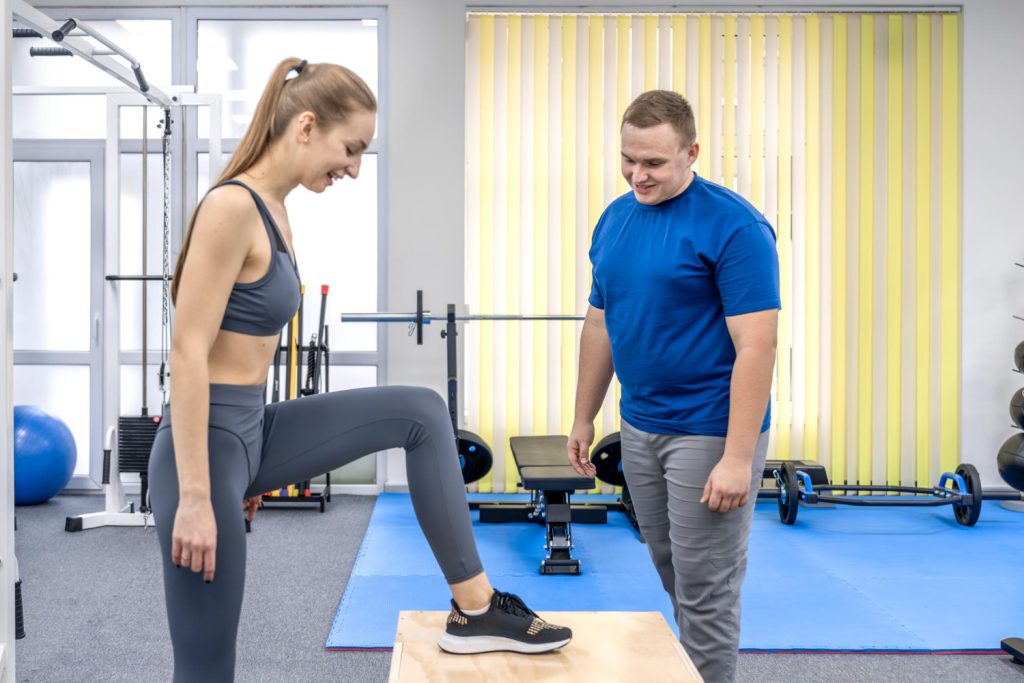 Trainer helping woman with dumbbell shoulder press exercise in gym