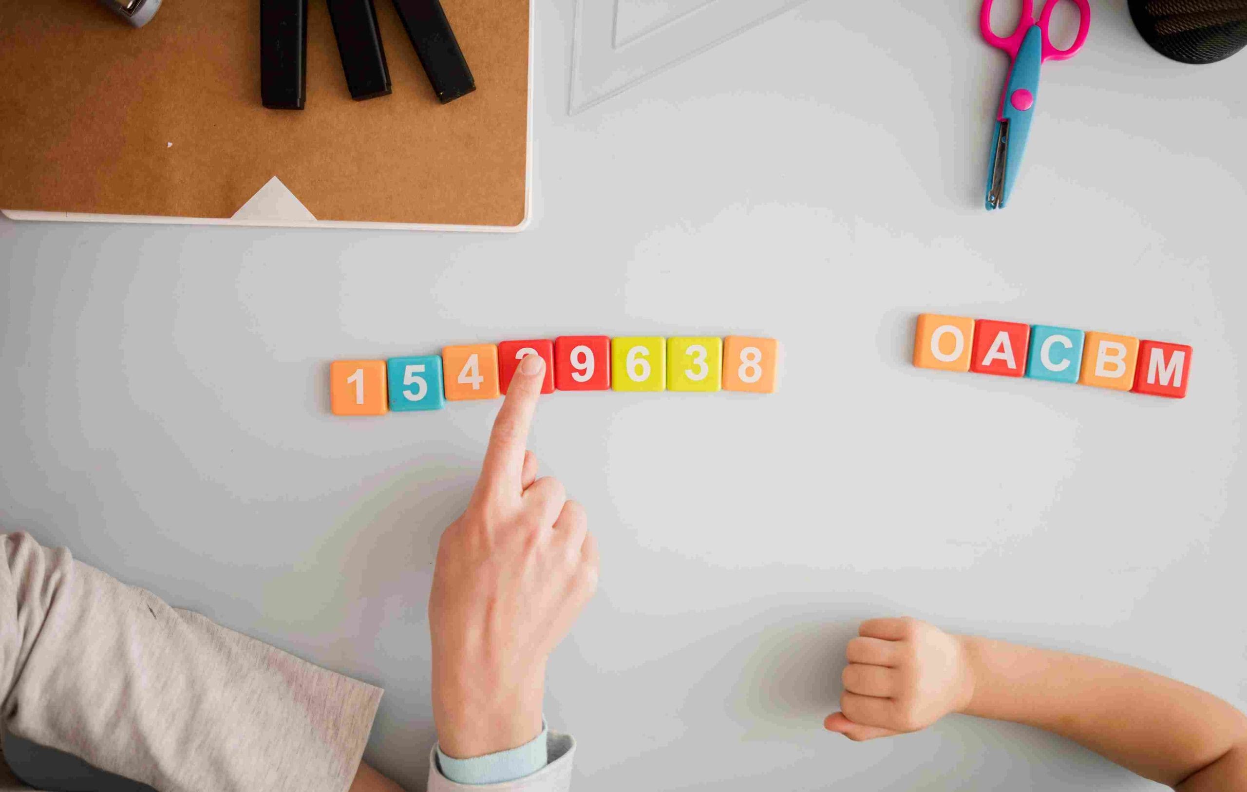 A child's hand pointing at colourful number and letter blocks, representing verbal reasoning.
