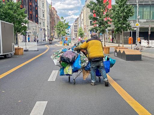 A picture of a homeless person from behind, walking down the road with all of their belongings on a cart